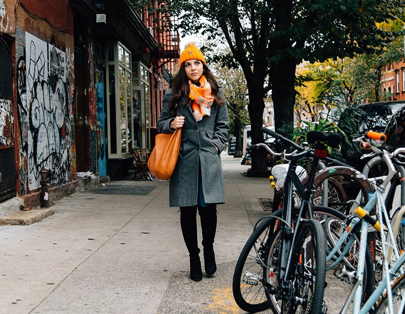 A woman in an orange winter hat walks down a city sidewalk
