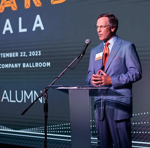 A man stands at a podium in front of a microphone during the Alumni Awards Gala
