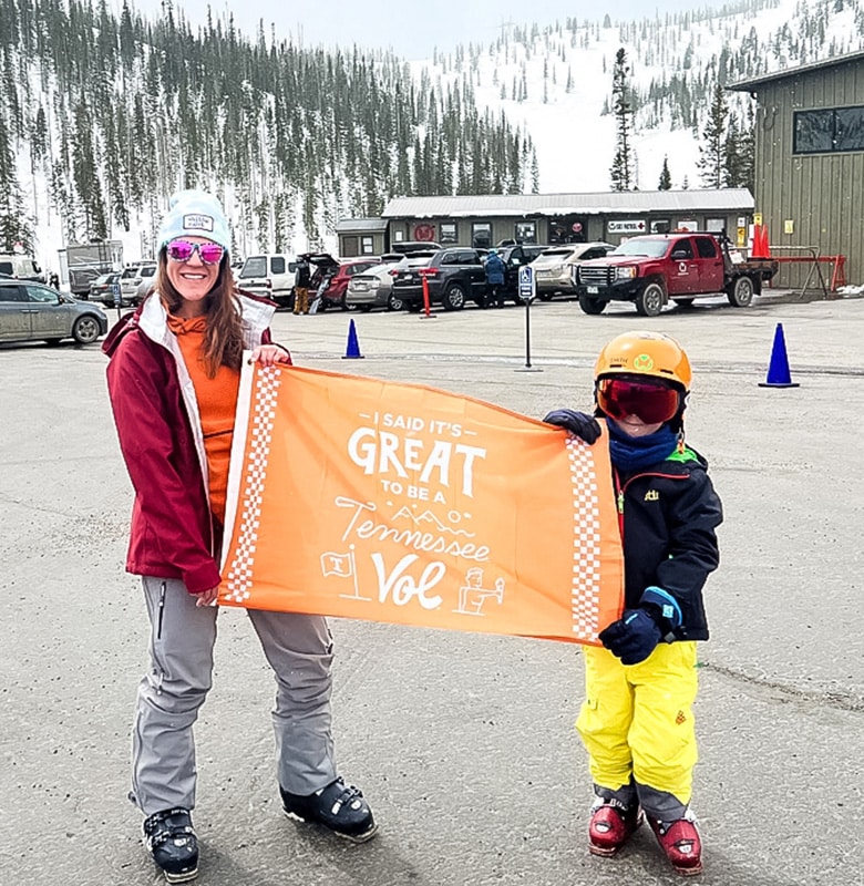 An alumna and a child hold a Tennessee Volunteers flag with snowy mountains in the background