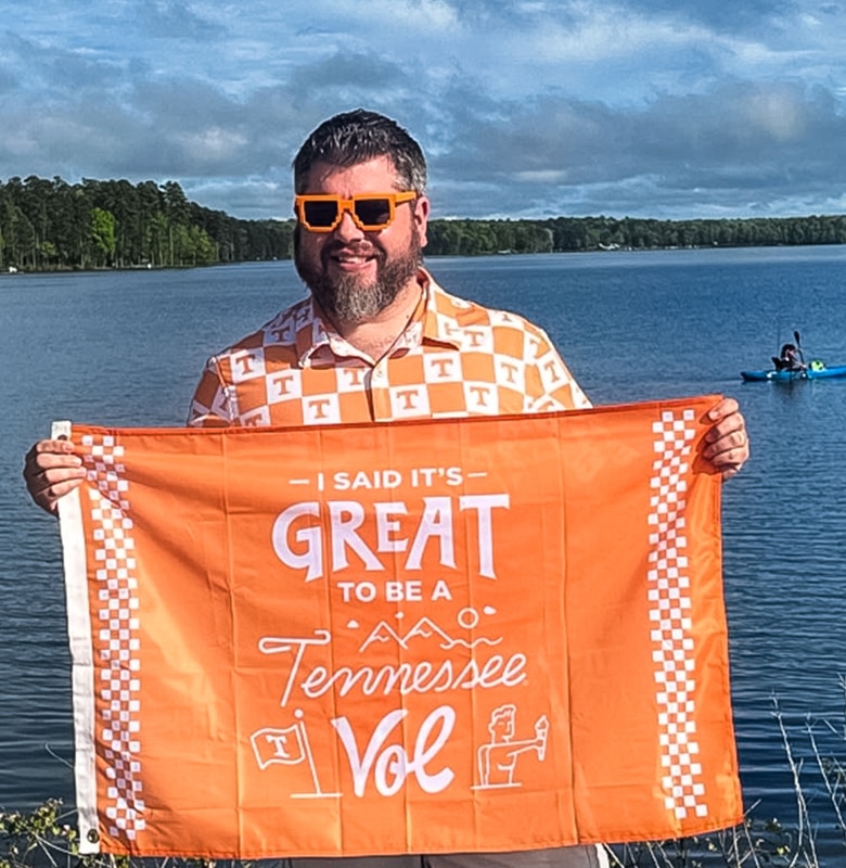 An alumnus holds a Tennessee Volunteers flag in front of a body of water