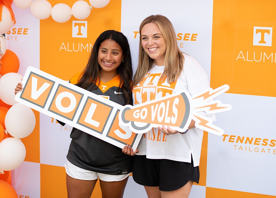 Two females hold Vols-themed signs in front of an orange-and-white checkered backdrop