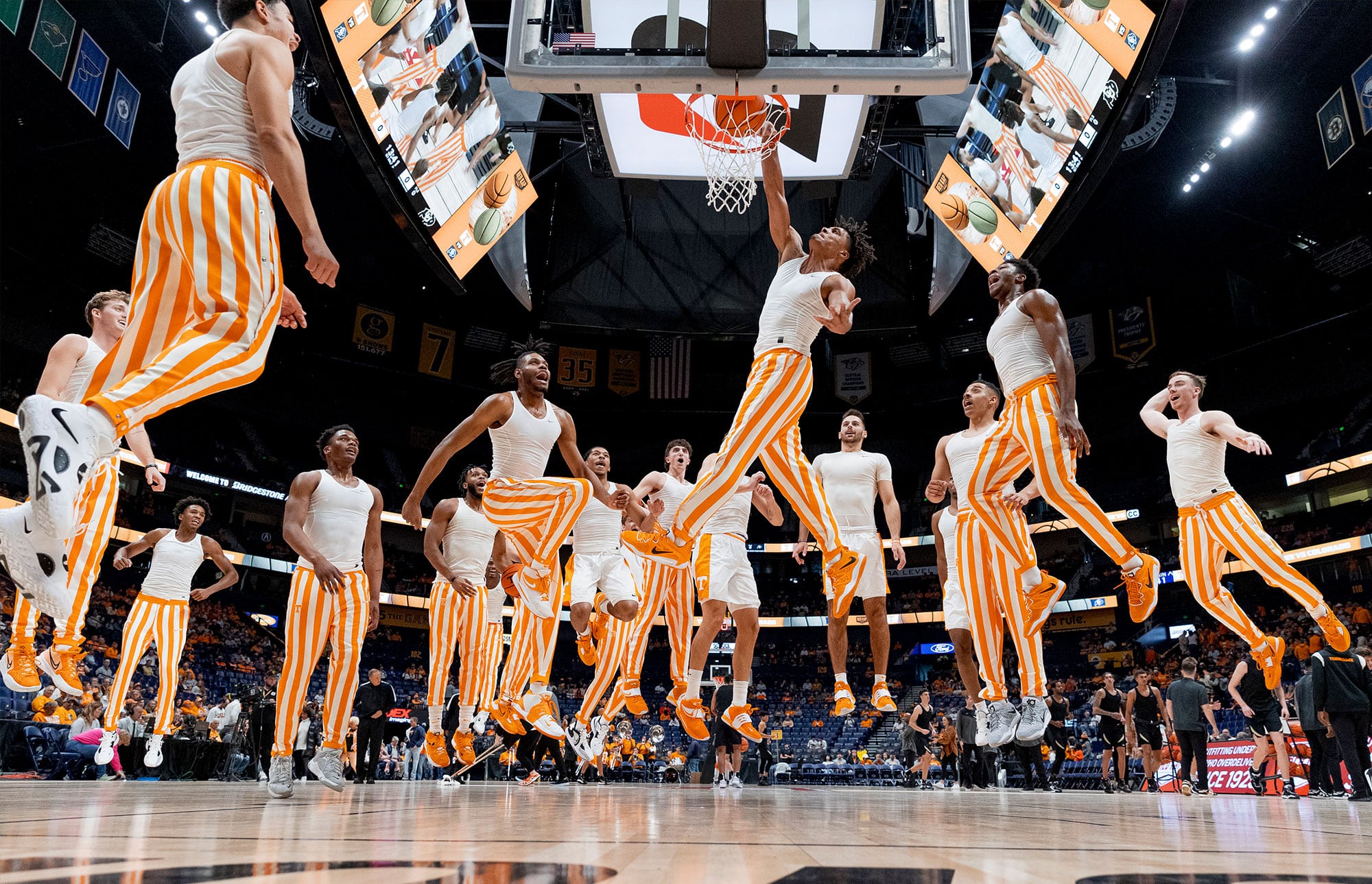The men's basketball team jumps as one team member makes a slam dunk