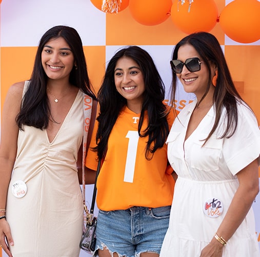 Three women pose in front of an orange-and-white checkered backdrop