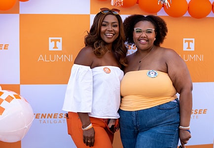 Two alumna pose for a photo against a checkered backdrop during a Tennessee Tailgate