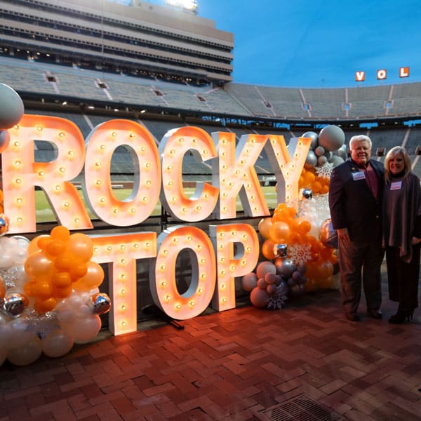 Two alumni pose next to lighted letters that spell Rocky Top in Neyland Stadium