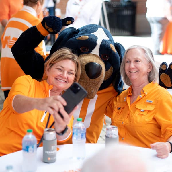 Two alumni take a selfie with Smokey during a Tennessee Tailgate