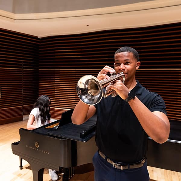 In the foreground a student plays the trombone as another student plays the piano in the background