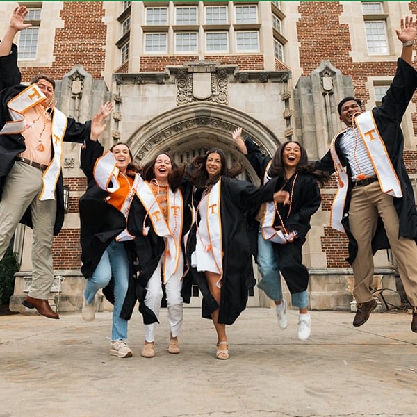 Six students in UT commencement regalia jumping