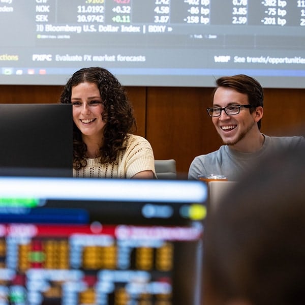 Two students looking at a computer monitor. In the foreground is a different computer monitor with numbers.