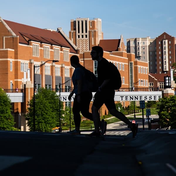 The silhouette of two students walking in front of the Haslam College of Business and the Ped Walkway bridge