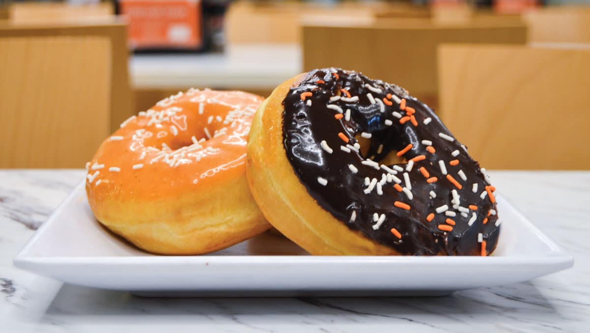 Two doughnuts on a plate, one has orange icing and one has brown icing