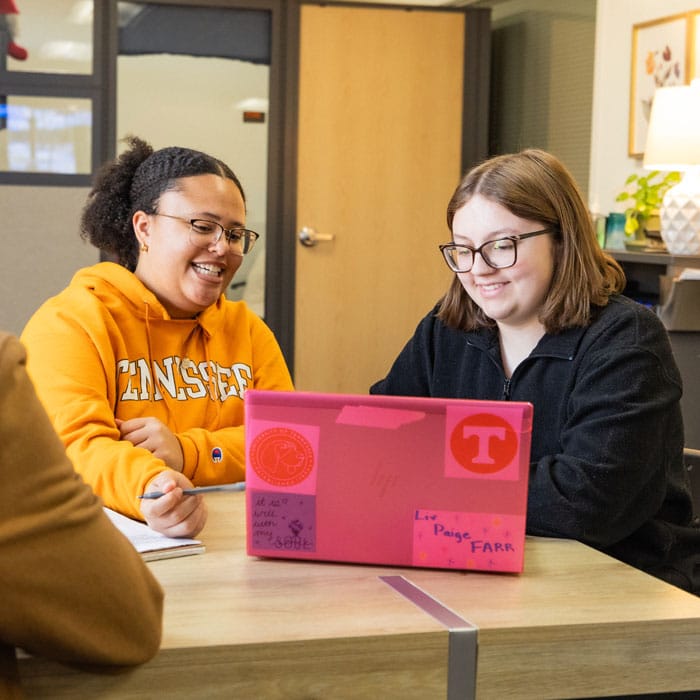 Madison Howard and student Olivia Farr look at the screen of a pink laptop