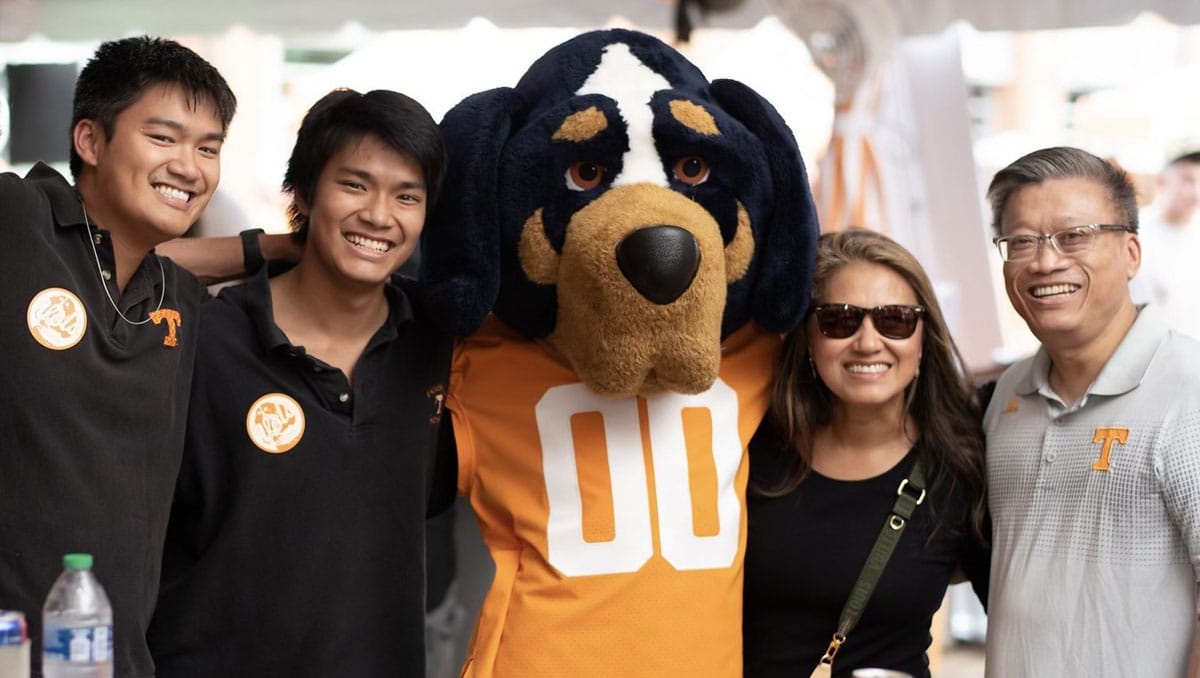 Denise Tran, Jonathan Mai, and their two sons pose for a photo with the Smokey mascot during a 2023 UT alumni tailgate.