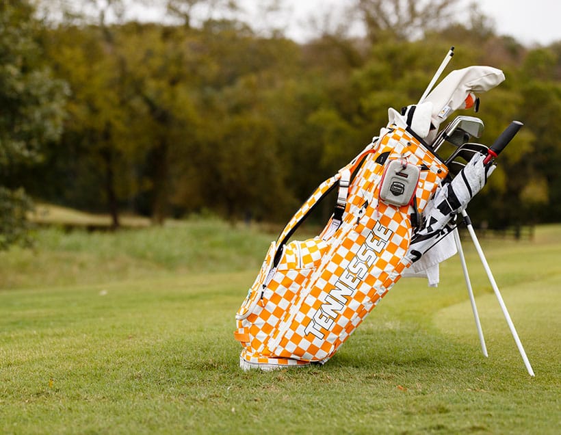 An orange-and-white checkered golf bag on a green golf course