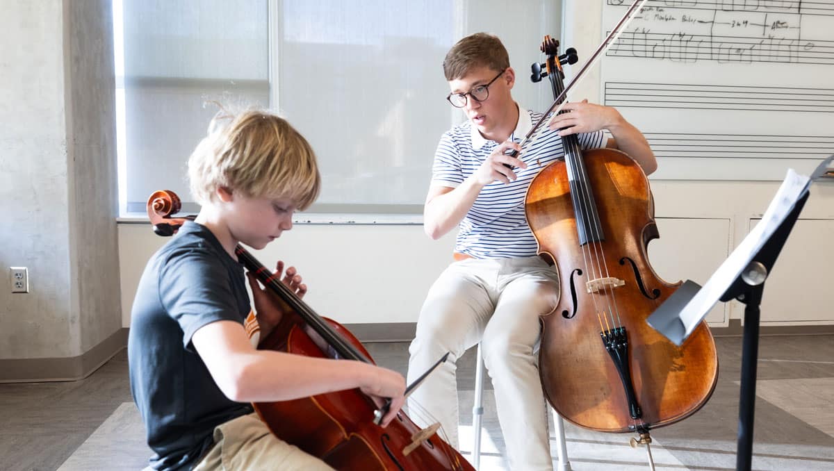 Stephen Arthur helps a young student learn to play the cello.