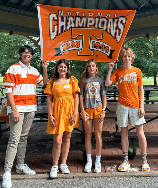 Four incoming students pose for a photo under a UT branded championship banner.