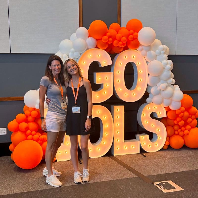 marden-kim-and-powell-kyra-orientation-800x800 Kim Marden and Kyra Powell stand next to an orange-and-white balloon arch and lighted letters that say Go Vols during Kyra's student orientation.