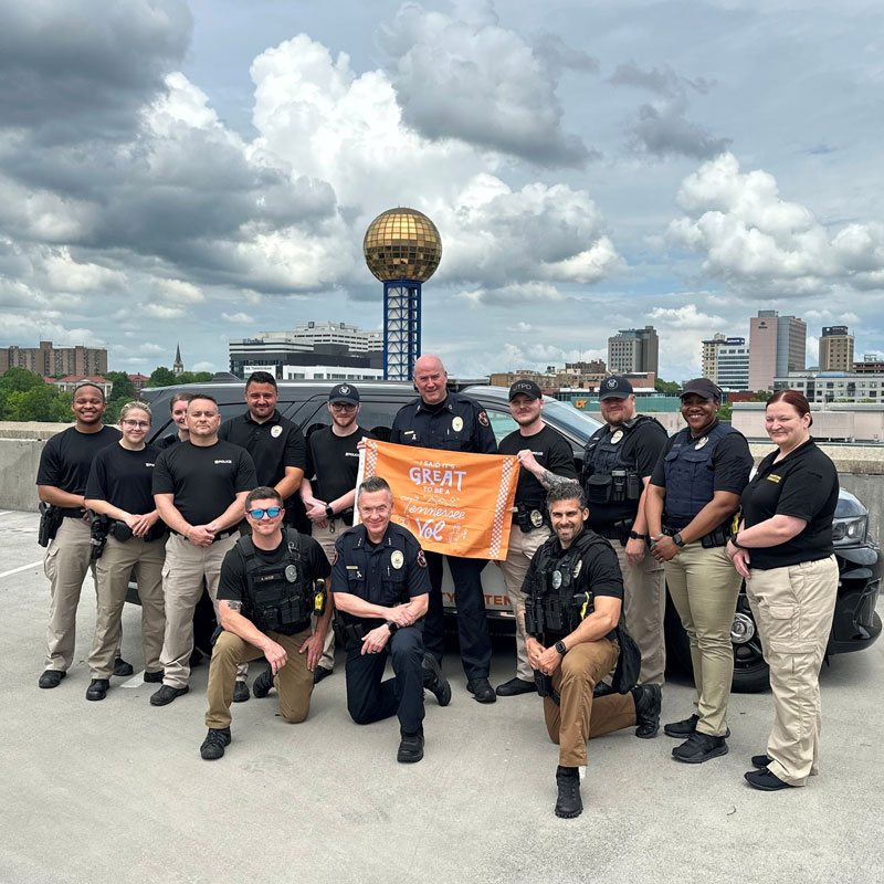 new-vol-day-800x800-2 A group of people pose with the It's Great to Be a Tennessee Vol flag. The Sunsphere and Knoxville skyline are visible in the background.