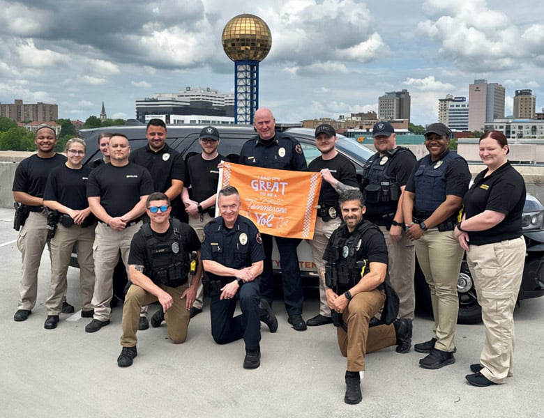 alumni-new-vol-4 A group of people pose with the It's Great to Be a Tennessee Vol flag. The Sunsphere and Knoxville skyline are visible in the background.