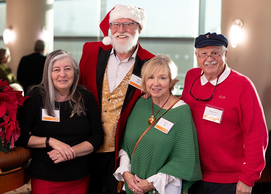 hero-retirees Four retirees pose for a photo during the annual holiday party. One man has a white beard and red hat like Santa.