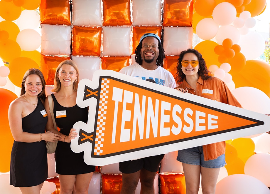 hero-young-alumni Four young alumni hold a giant orange Tennessee pendant in front of an orange-and-white balloon background.