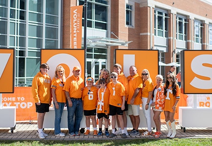 Eleven family members wearing Tennessee orange stand together for a photo in front of the V-O-L-S letters during a tailgate.