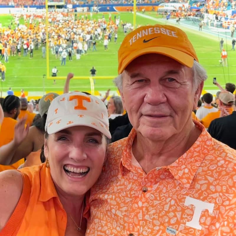 vantrease-jana-and-jerry-football-game-800x800 Jana Vantrease and Jerry Vantrease smile for a photo with a Tennessee football game behind them.