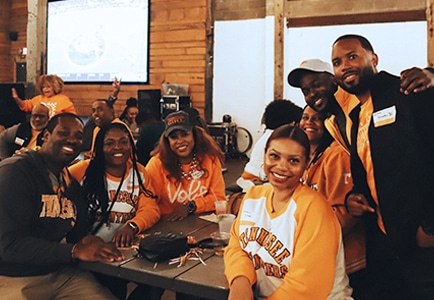 A group of seven alumni around a table pose for a photo.