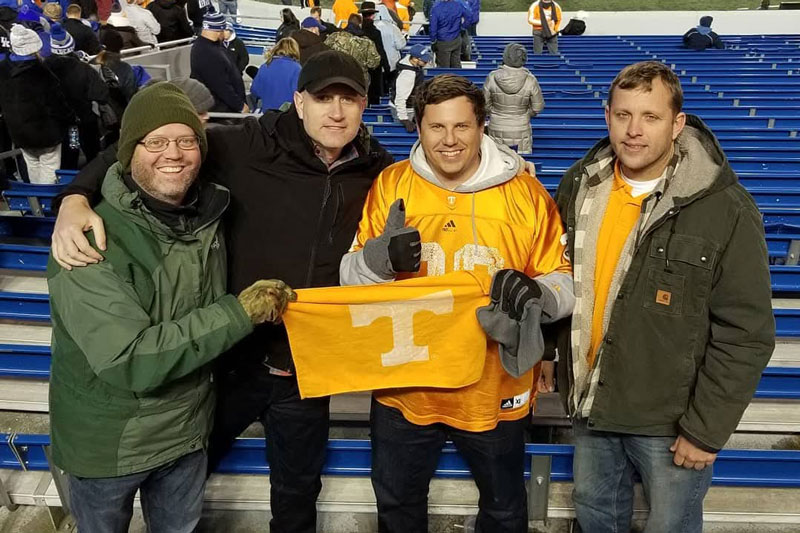 Four friends dressed in cold-weather apparel pose for a photo while holding an orange Tennessee flag.