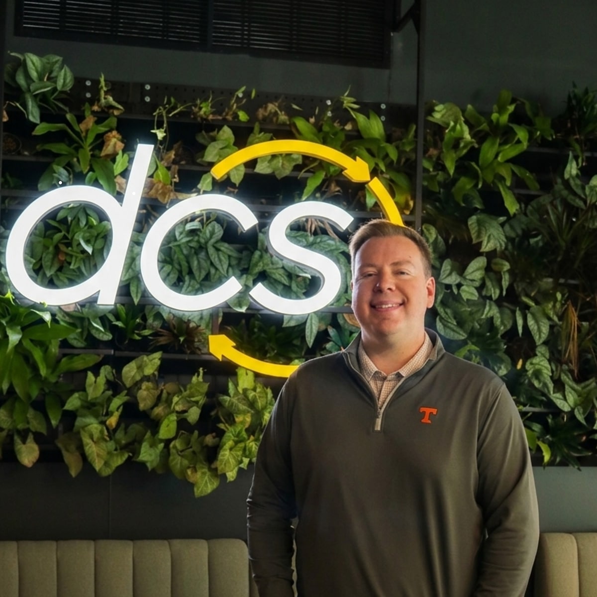 Wiley Stidham smiling in front of a neon sign that say "DCS"