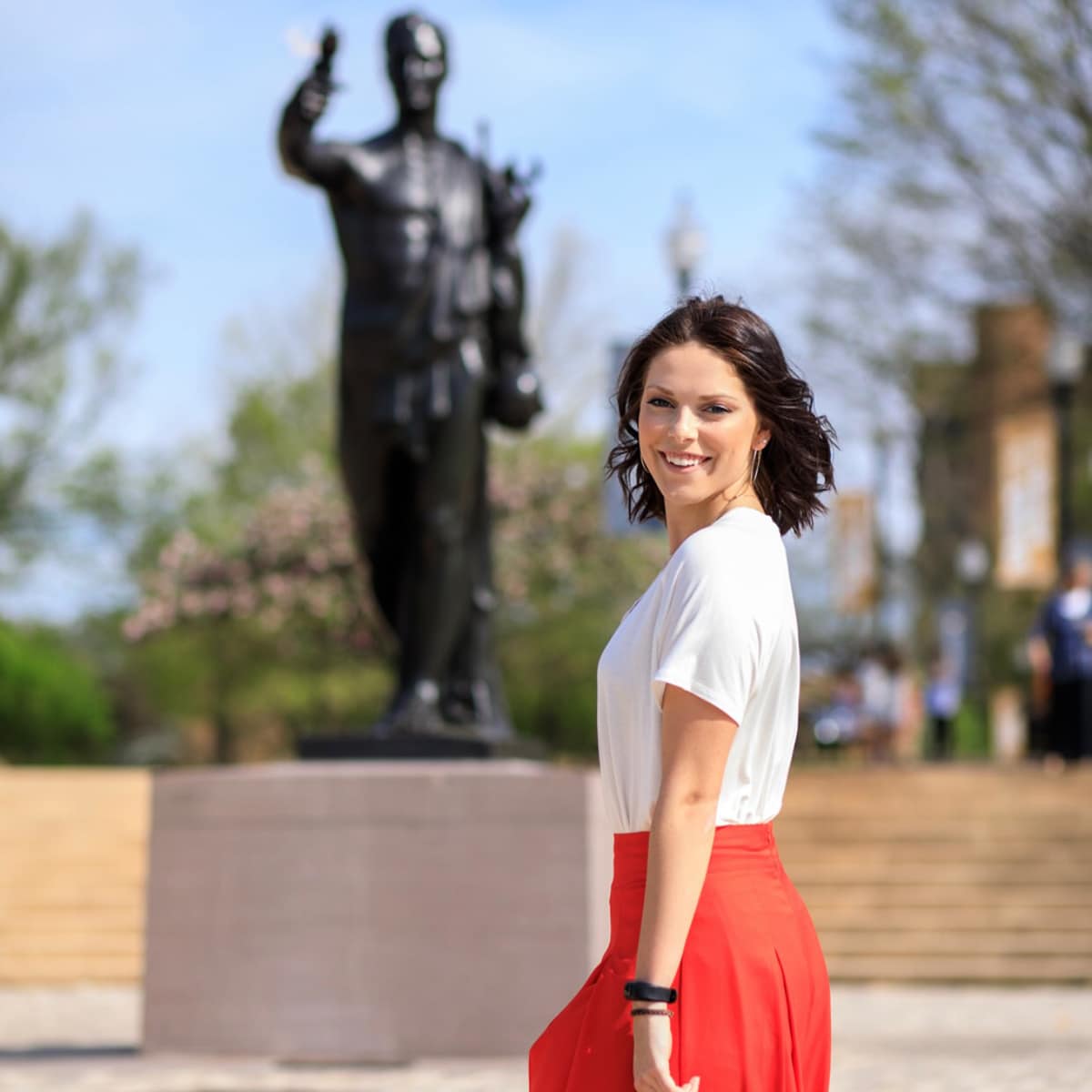 Graduation-&-Torchbearer-statue Person in front a a statue smiling