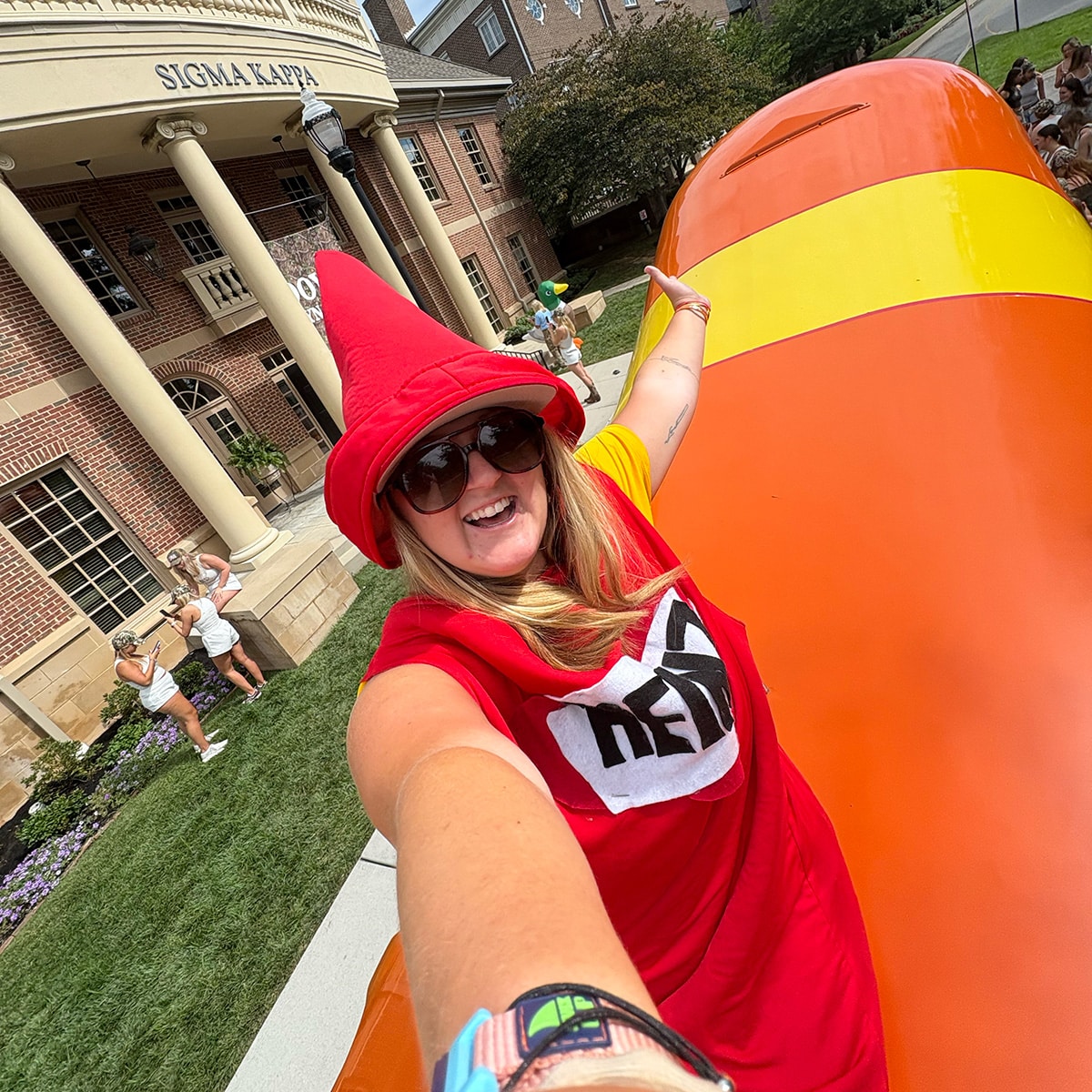 Person in katchup costume on smiling with building behind them