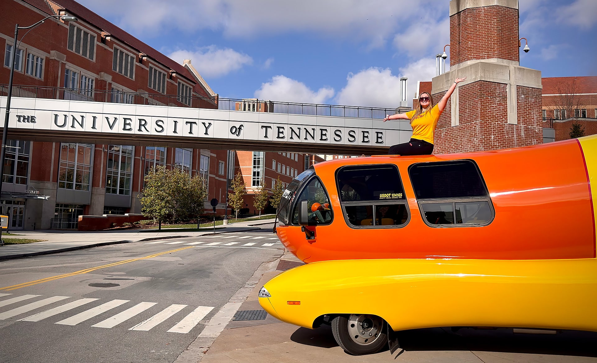 Oscar Meyer Wienermobile with person sitting on top of it in front of University of Tennessee campus bridge