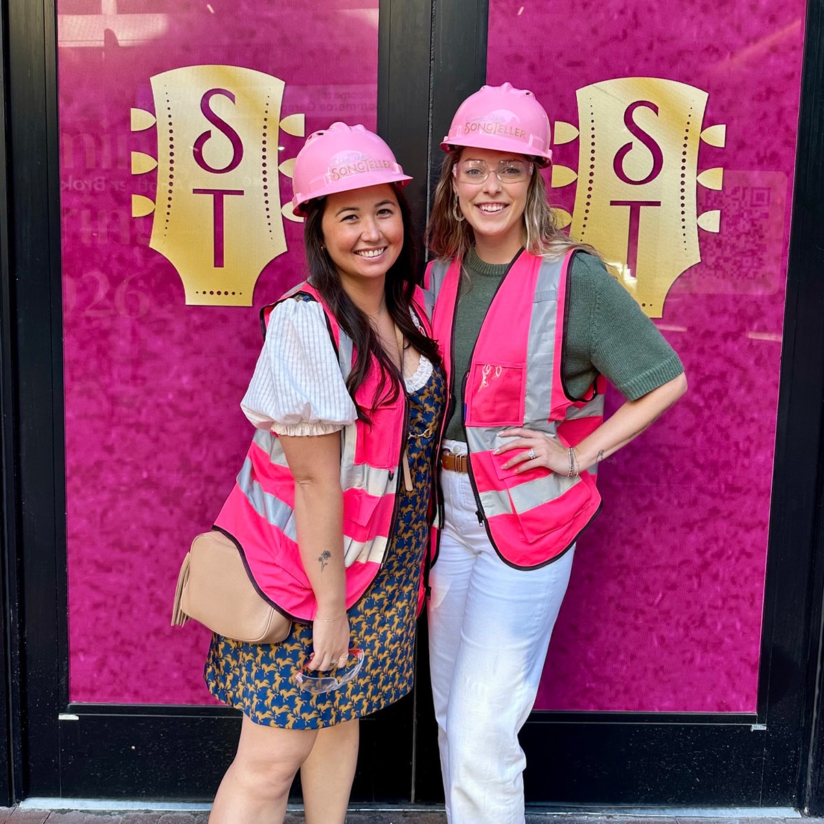 Songteller-Construction-2 Two people in pink construction hats smiling in front of doors with pink background