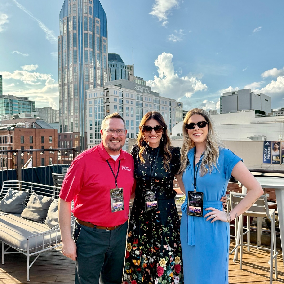 Songteller-Industry-Conference-2 Three people in business clothes on a rooftop smiling with the cityscape behind them