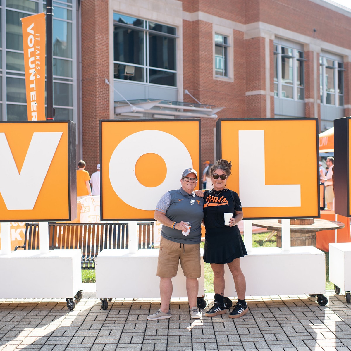 Two people smiling in front of sign that says VOL